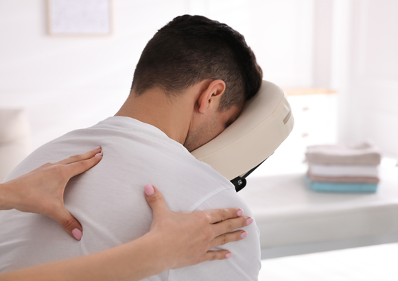 A man receiving a massage in a chair designed for massage from a massage therapist at a corporate event